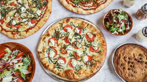 Overhead view of assorted pizzas with fresh salads and a chocolate chip cookie on a restaurant table