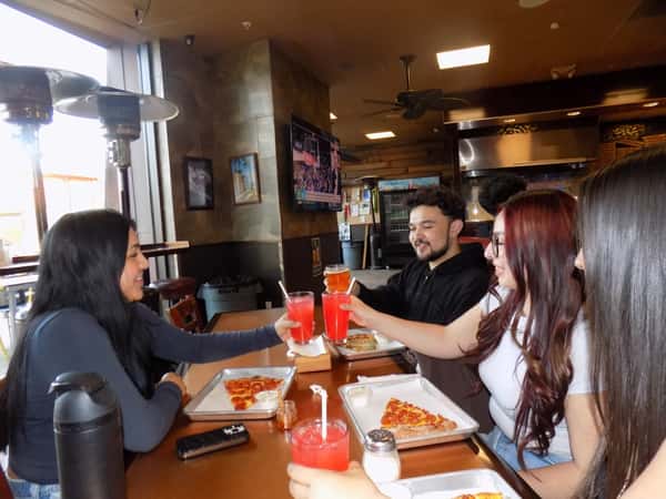 Group of friends toasting colorful drinks over pizza slices at a casual pizzeria table