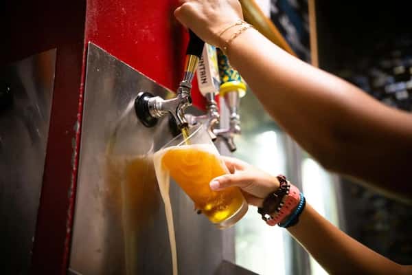 Bartender pouring golden draft beer from tap into a glass at a lively bar