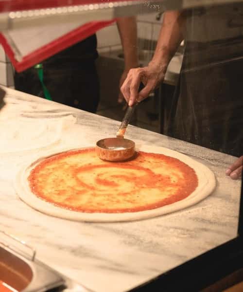 Pizza chef spreading tomato sauce on fresh dough in a pizzeria kitchen