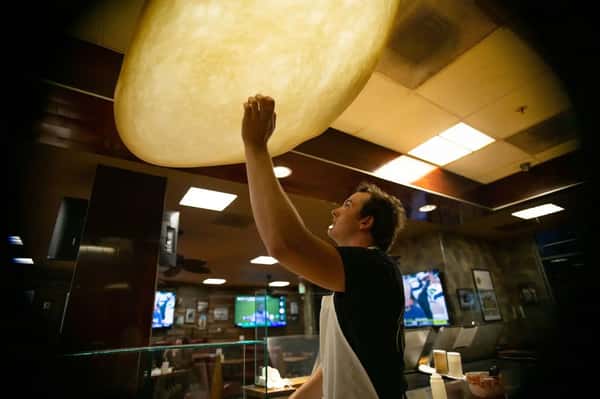 Pizza chef stretching and tossing large dough in the air inside a casual pizzeria