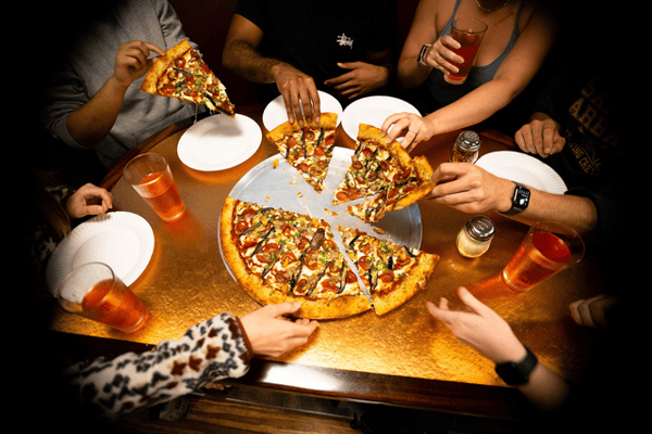 Group of friends sharing large pizza with assorted toppings around a restaurant table