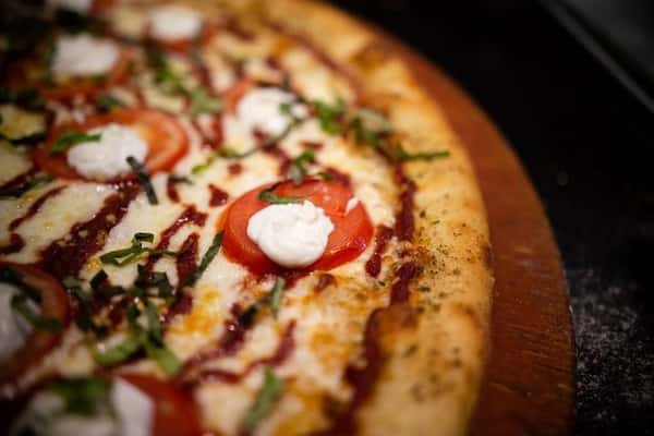 Close-up of freshly baked pizza with melted mozzarella, tomato slices, and basil on crispy crust