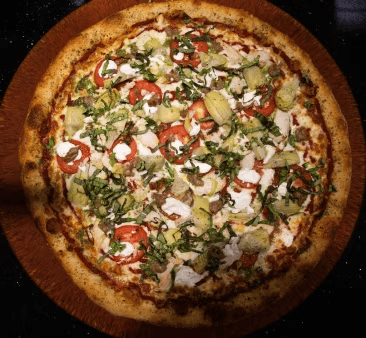 Overhead view of gourmet white pizza topped with tomatoes, artichokes, herbs, and melted cheese on a crispy crust