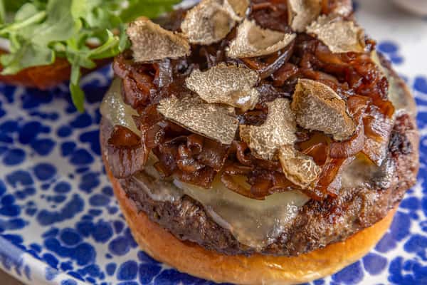 Close-up of a gourmet burger topped with caramelized onions, melted cheese, and shaved black truffles on a toasted bun.