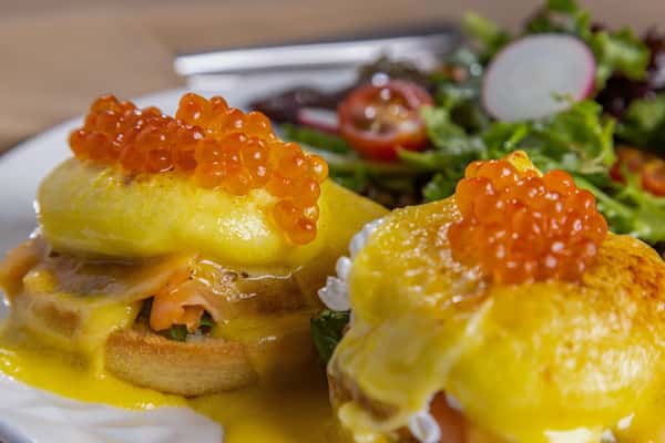 Close-up of eggs Benedict topped with salmon roe and hollandaise sauce, served with a fresh side salad.