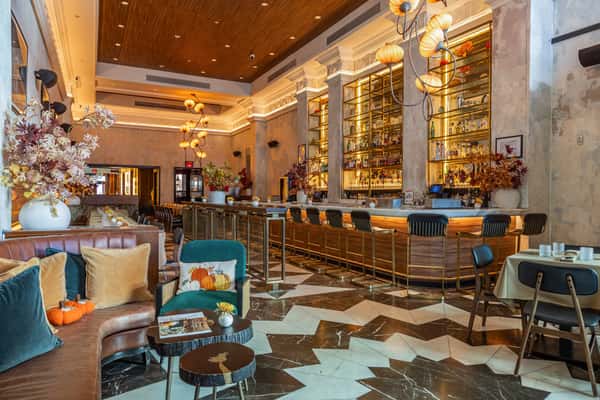 Elegant bar interior featuring a long marble counter, gold-accented bar stools, floral arrangements, and backlit liquor shelves.