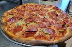Classic pepperoni pizza with jalapeños and melted cheese on a crisp golden crust, served on a raised metal stand.
