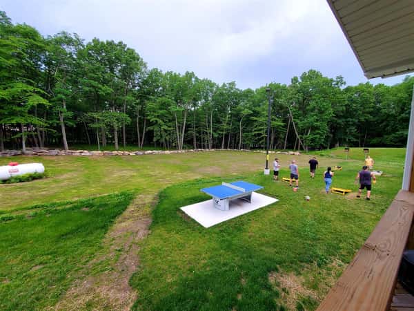 yard surrounded by trees with people playing cornhole