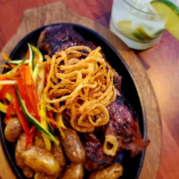 skillet with meat and potatoes topped with onion straws and veggies