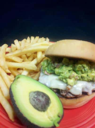 cheeseburger topped with guacamole and a side of french fries