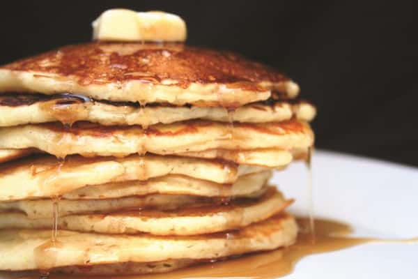 tall stack of pancakes topped with butter and syrup