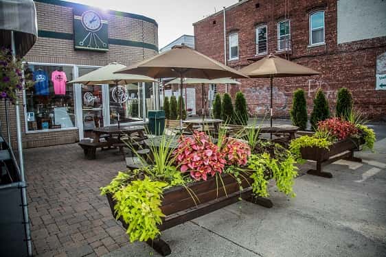 outside view of stella's with picnic tables covered with umbrellas and various flowers and plants