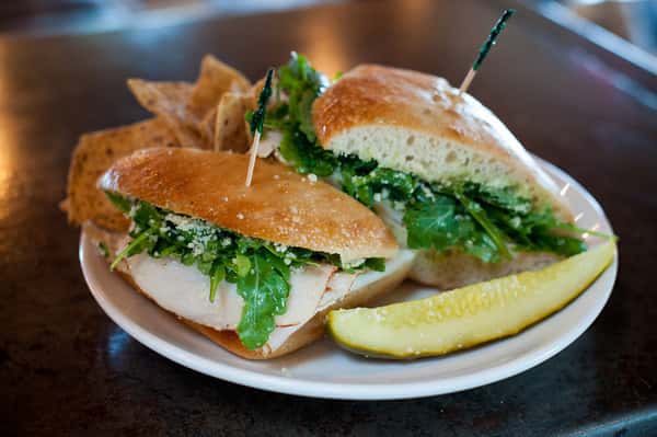 Grilled chicken sandwich with greens on toasted bun served with chips and pickle spear