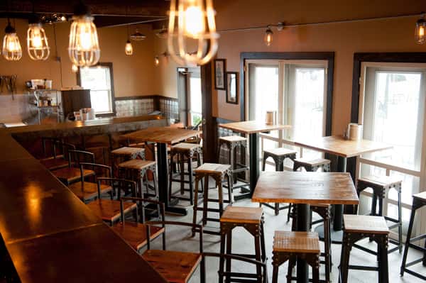 Cozy restaurant bar interior with high-top tables, wooden stools, and warm pendant lighting