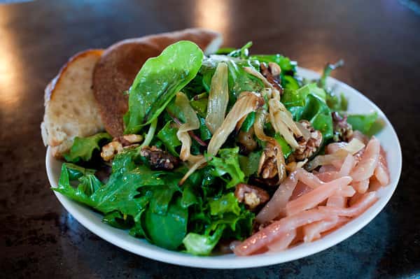 Fresh green salad with mixed greens, pickled onions, candied pecans, and toasted bread slice on a plate