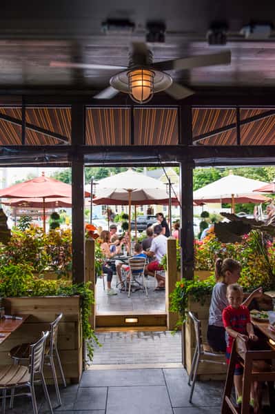 View from inside restaurant looking out to lively outdoor patio with umbrellas, greenery, and guests dining