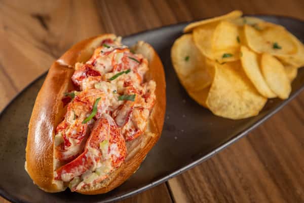 A classic lobster roll in a split-top bun served with a side of potato chips.