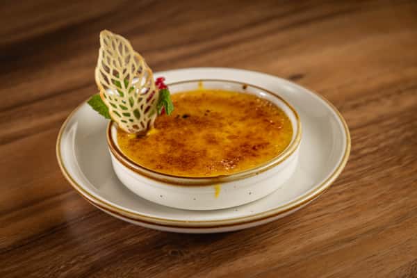 A ramekin of crème brûlée with a caramelized sugar crust, garnished with a dried fruit chip and mint