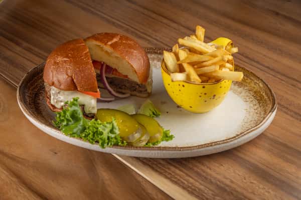 A burger served on a bun with lettuce and tomato, accompanied by fries and a grilled lemon.