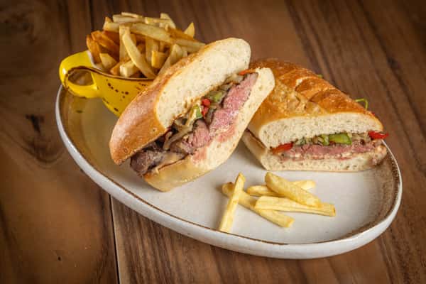 A baguette sandwich filled with sliced steak and peppers, served with french fries.