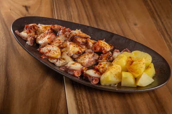 A variation of the grilled octopus dish, featuring tentacles and potatoes on a dark platter.