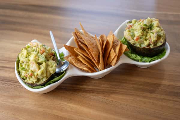 A curved serving dish holding tortilla chips, guacamole, and salsa.