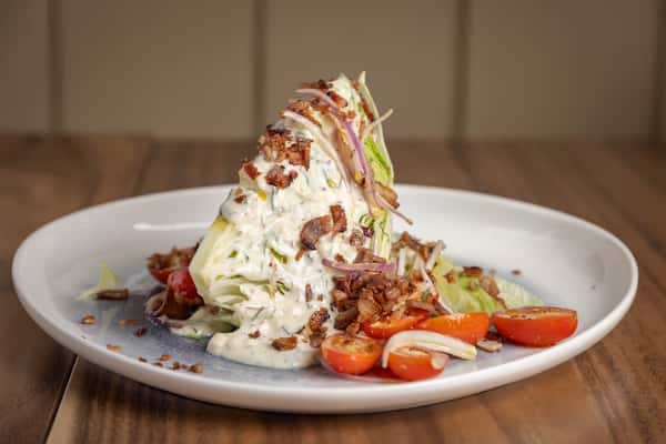 A wedge of iceberg lettuce topped with creamy blue cheese dressing, bacon bits, and cherry tomatoes.