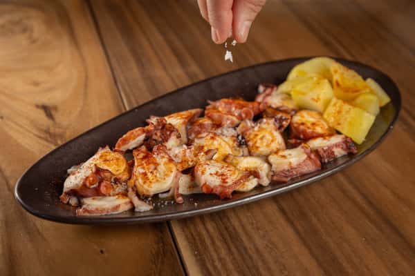Grilled octopus tentacles served on a dark oval plate with roasted potatoes.