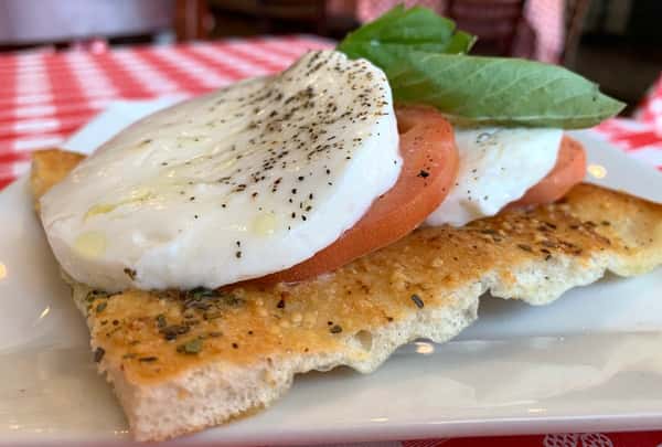Fresh Caprese flatbread with creamy mozzarella, ripe tomato slices, basil leaves, and cracked black pepper atop toasted Italian focaccia.