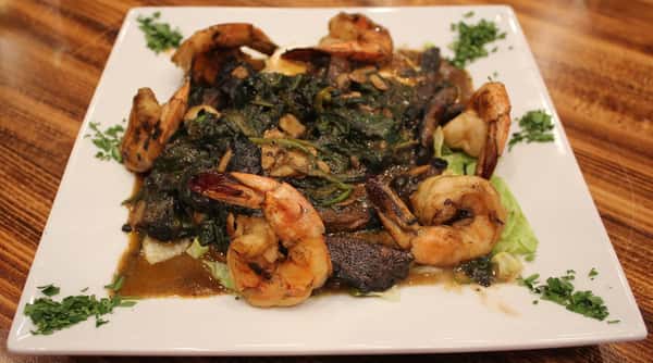 Garlic shrimp sautéed with spinach and mushrooms in a savory sauce, plated on a bed of cabbage and garnished with fresh herbs.