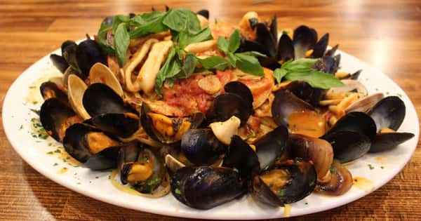 Seafood marinara featuring mussels, clams, calamari, and shrimp in a zesty tomato garlic sauce, topped with fresh basil on a large white plate.