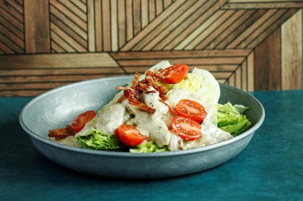 Classic wedge salad with iceberg lettuce, cherry tomatoes, crispy bacon, and creamy blue cheese dressing, served in a rustic gray bowl.
