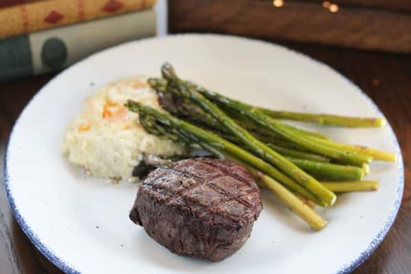 Grilled filet mignon with charred grill marks, served with mashed potatoes and roasted asparagus on a rustic white plate.