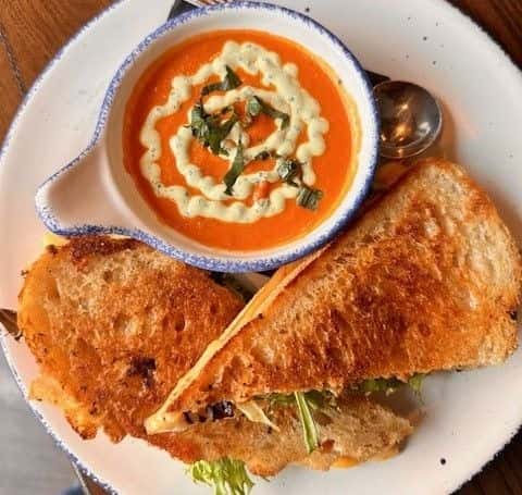 Golden toasted grilled cheese sandwich paired with creamy tomato soup topped with basil and a swirl of cream, served in a rustic ceramic bowl and plate.