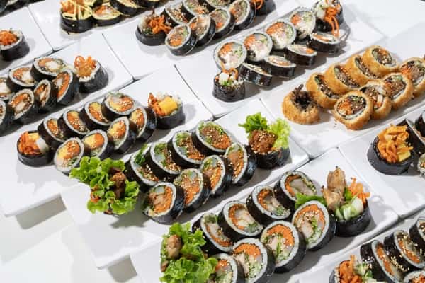Assorted Korean gimbap rolls neatly arranged on white rectangular plates, showcasing various colorful fillings.