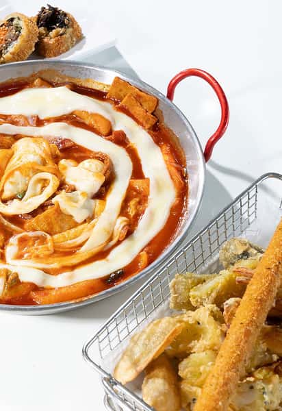 Korean tteokbokki in spicy red sauce topped with melted cheese, served with assorted crispy fried tempura sides.