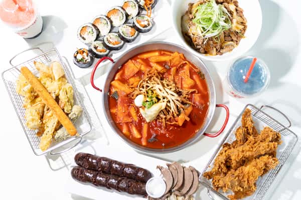 Korean feast with spicy tteokbokki, kimbap rolls, fried chicken, assorted tempura, soondae, bulgogi rice bowl, and colorful drinks.