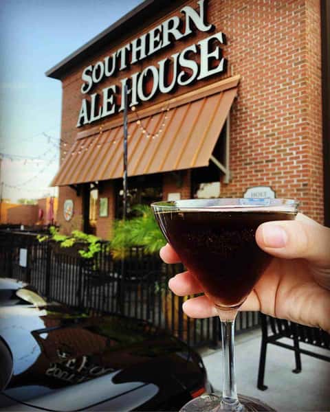Hand holding cocktail in front of Southern Ale House
