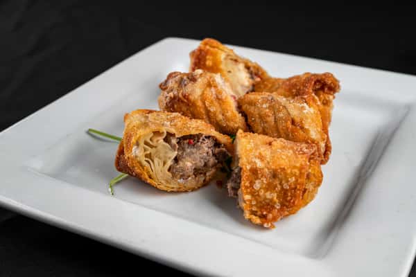 Golden fried beef egg rolls filled with savory ground beef and veggies, halved to show the filling, served on a square white plate with a green garnish.