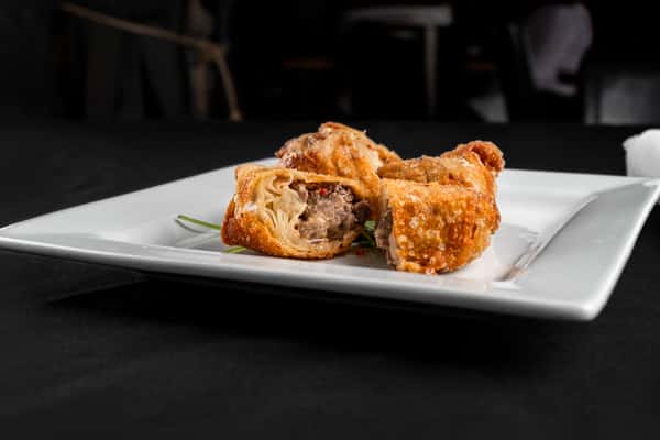 Golden fried beef egg rolls with a crispy wrapper and savory filling, cut in half and served on a square white plate with a garnish.