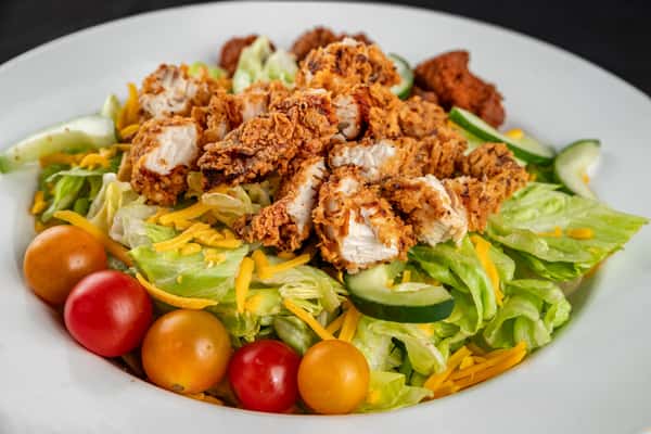 Southern-style fried chicken salad with crispy iceberg lettuce, grape tomatoes, shredded cheddar cheese, and cucumber slices, served in a white bowl