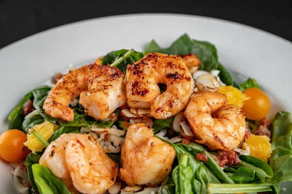 Grilled shrimp spinach salad featuring tender shrimp atop fresh baby spinach, sliced almonds, cherry tomatoes, orange segments, and crumbled bacon, served in a white bowl for a vibrant and healthy Southern-inspired dish.