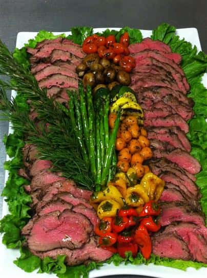 catering tray with sliced prime rib and various roasted vegetables with rosemary as a garnish