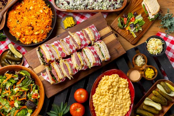 Catering spread, sandwiches on a wood platter surrounded by sides