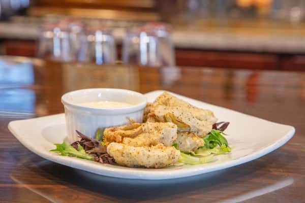 Crispy fried artichoke hearts with creamy dipping sauce and fresh greens served on a white plate at a bar
