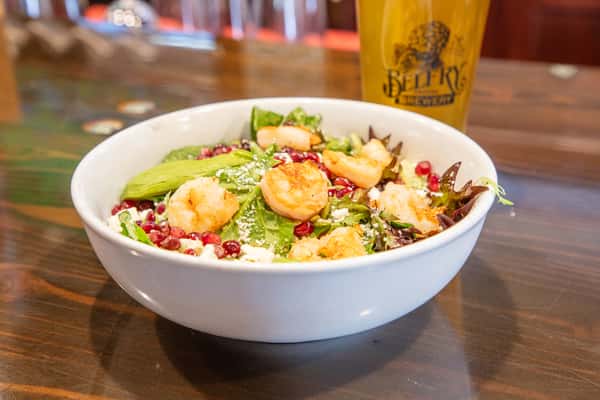 Shrimp and avocado salad with mixed greens, pomegranate seeds, and cheese served in a white bowl with a craft beer at a brewery restaurant