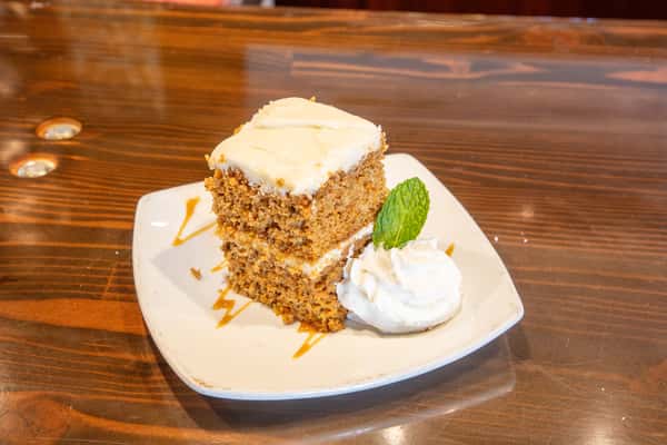 Moist carrot cake slice with cream cheese frosting, caramel drizzle, and whipped cream garnish on a dessert plate