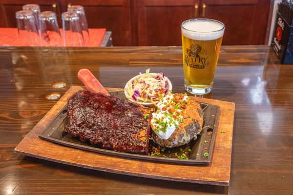 BBQ ribs platter with baked potato topped with sour cream and bacon, served with coleslaw and a craft beer at a brewery restaurant