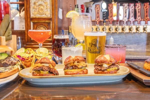 Assorted gourmet sliders with melted cheese and toppings served with craft beers and colorful cocktails on a brewery bar counter